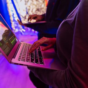 Two professionals analyzing data on laptops with colorful lighting, focusing on cybersecurity details.